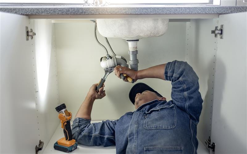 Plumber repairing pipes beneath a bathroom sink in Pompano Beach