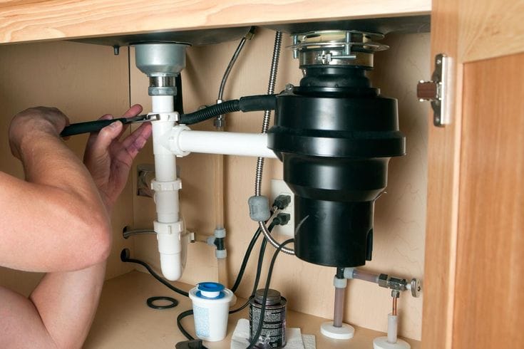 Plumber installing a garbage disposal beneath a kitchen sink in Pompano Beach