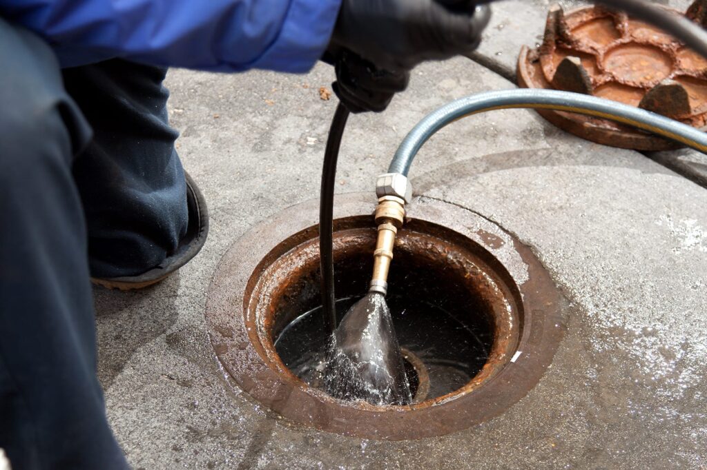 Plumber hydro jetting a sewer line through a manhole in Pompano Beach