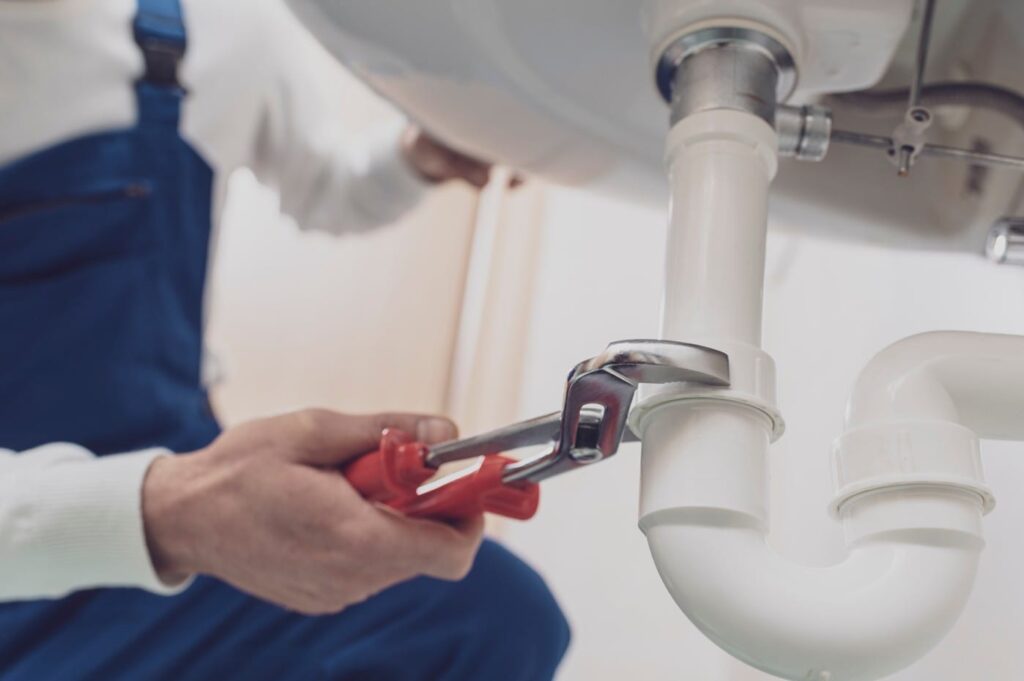 Plumber repairing a white drain pipe beneath a sink in Pompano Beach