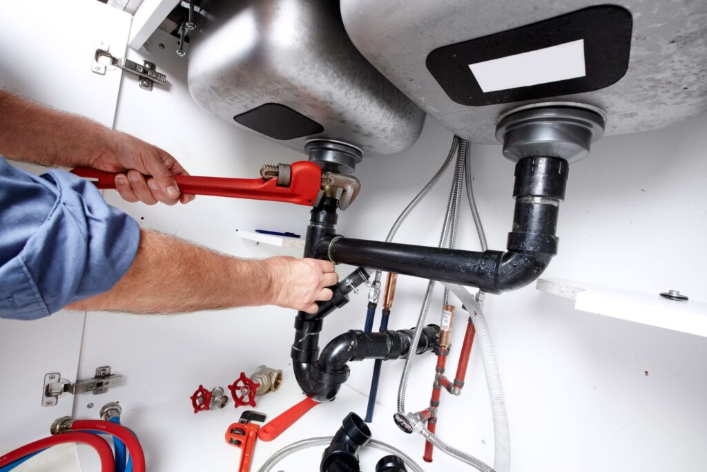 Plumber repairing drain pipes beneath a kitchen sink in Pompano Beach